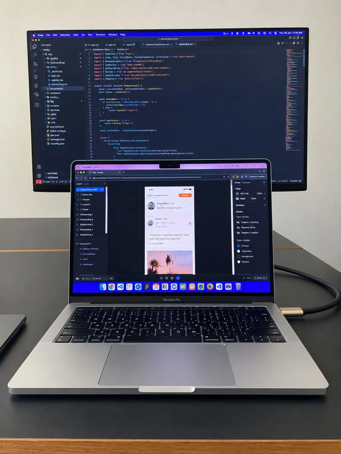 A laptop running an app, open in front of a large monitor filled with code.